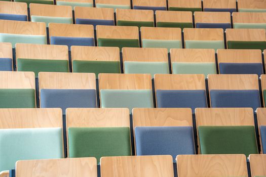 A pattern of colorful wooden chairs arranged in rows inside an empty auditorium.